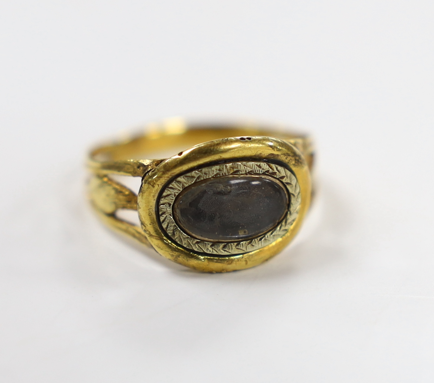 An early 19th century two colour yellow metal mourning ring, with glazed panel and pierced foliate shoulders, size R, gross weight 2.4 grams.